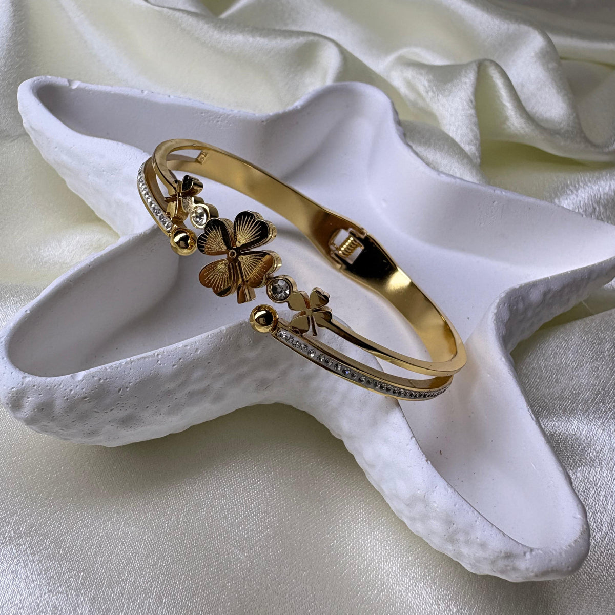 A gold-toned bangle bracelet with four-leaf clover charms and small clear stones,